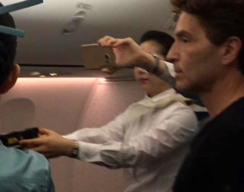 A Korean Air flight attendant holds a Taser gun as other passengers look on and the unruly passenger is subdued (Facebook)